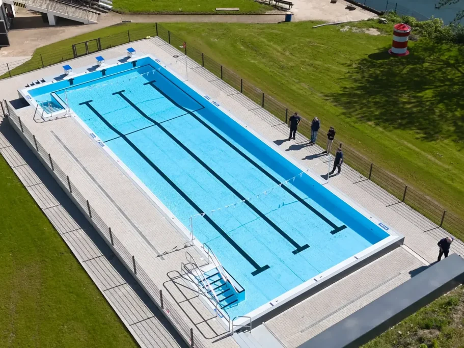 Schwimmbecken mit klar blauem Wasser und mehreren Bahnen, umgeben von Rasenflächen.