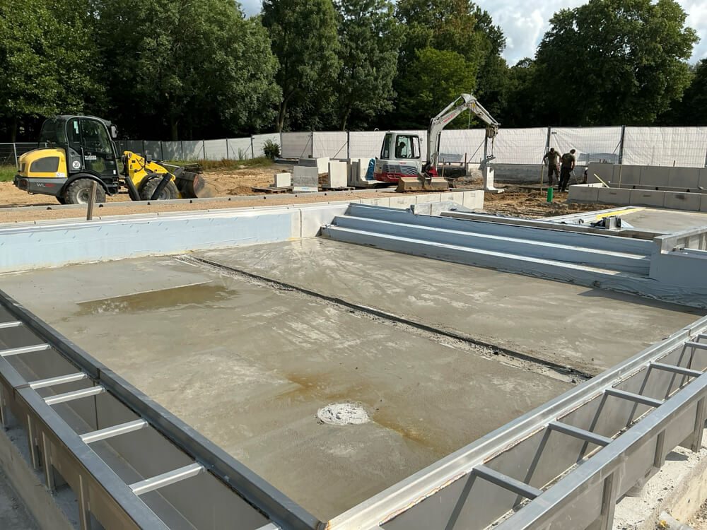 Blick auf eine Baustelle mit einem Fundamente für ein Schwimmbecken und Baustellenfahrzeugen.