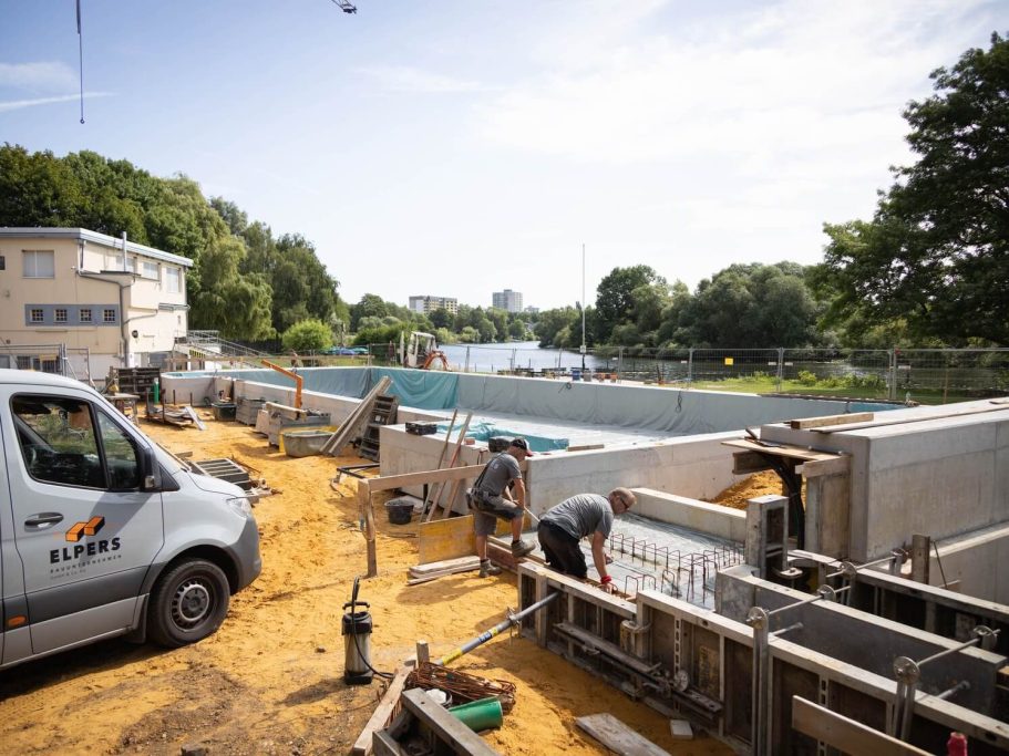 Bauarbeiten an einem Wasserbauprojekt mit Fahrzeugen und Arbeitern am Ufer.