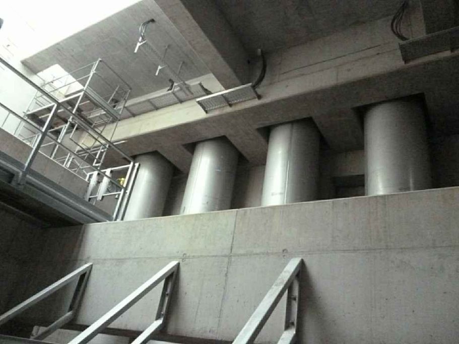 Drei silberne Behälter unter einer Decke aus Beton, mit einer Metalltreppe im Vordergrund.