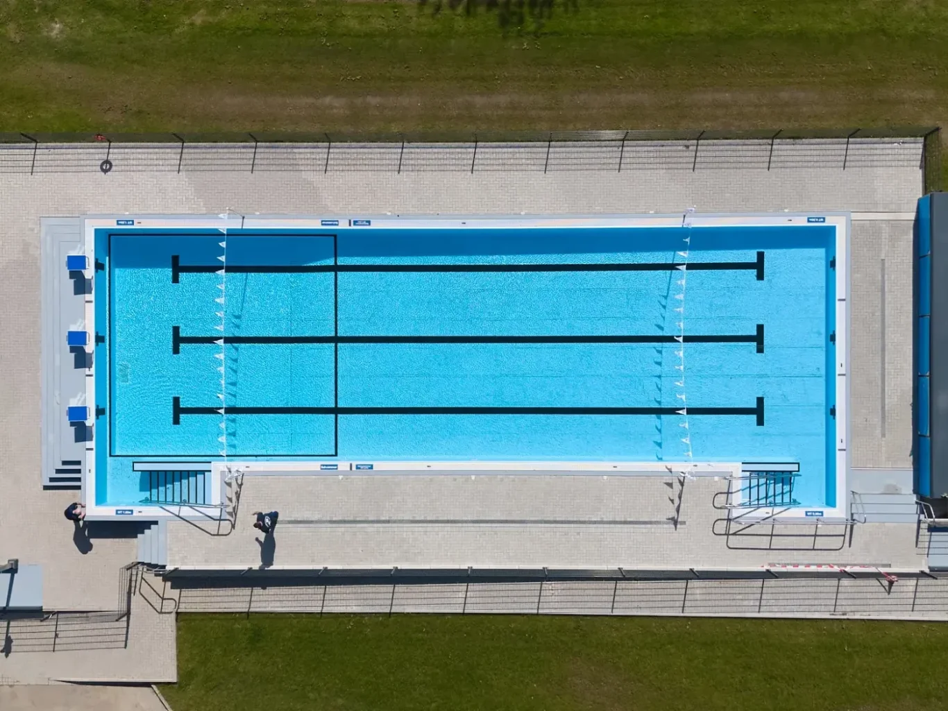 Schwimmbad mit mehreren Bahnmarkierungen und grünem Rasen rundherum.