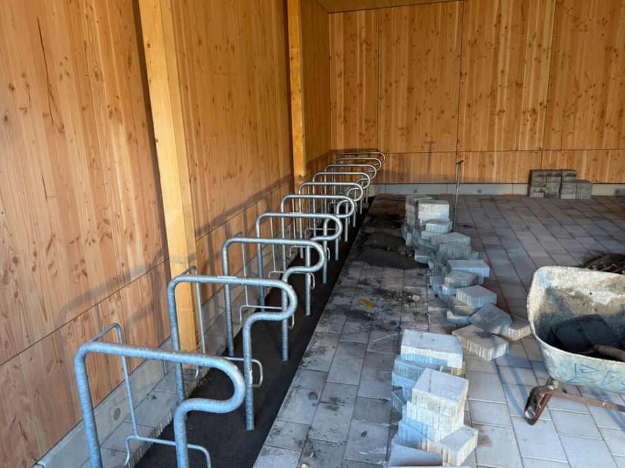 Reihe von metallenen Fahrradständern in einem halboffenen Raum mit Holzverkleidung.