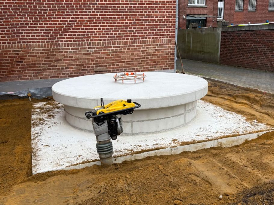Runde Betondecke mit kreisförmiger Öffnung auf Baustelle, umgeben von Erde.