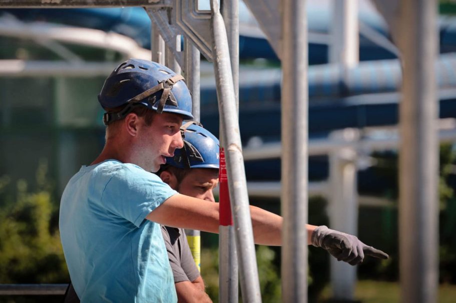 Zwei Bauarbeiter in Helmen, einer zeigt auf eine Baustelle im Hintergrund.