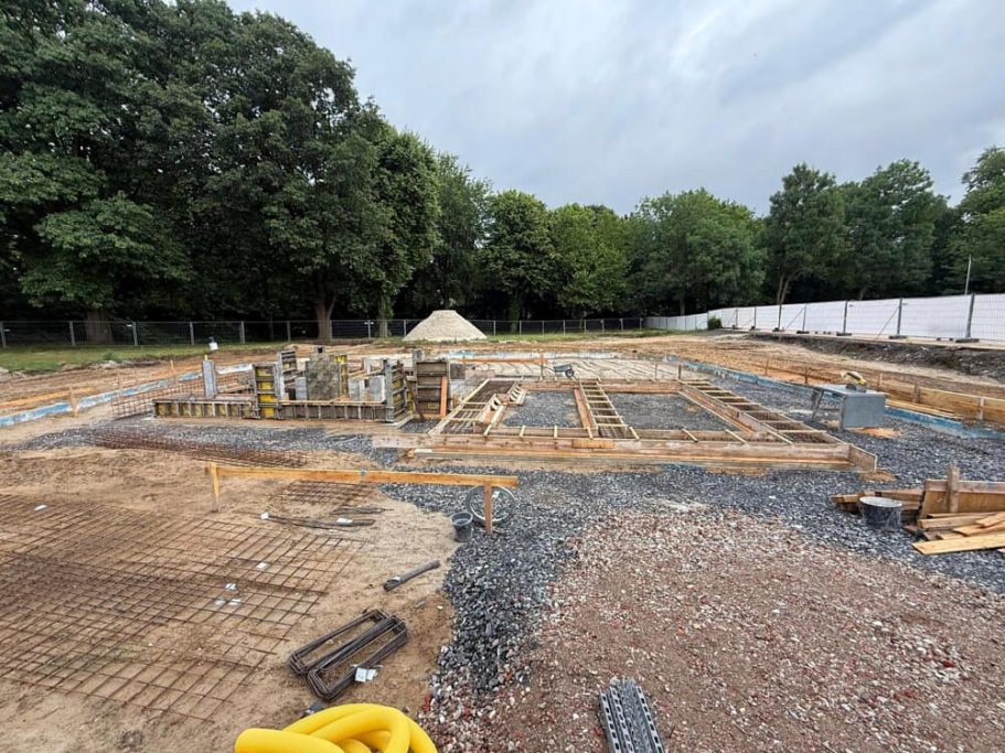 Baugelände mit Fundamentarbeiten, Holzrahmen und umgebendem Gelände.